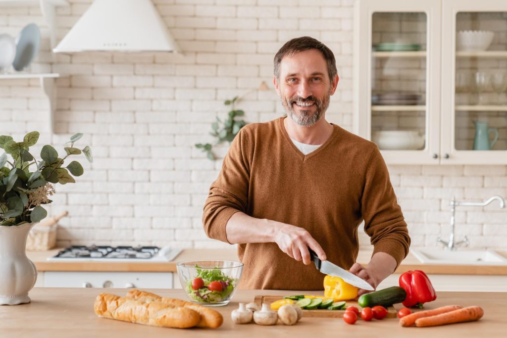Hombre sonríe mientras corta verduras